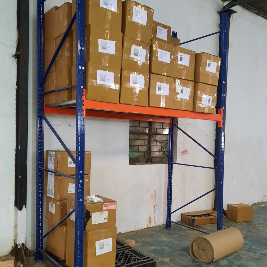 Warehouse Racks in Noida which are blue and orange in colour and have boxes on it with no base level, pallets are kept with more boxes