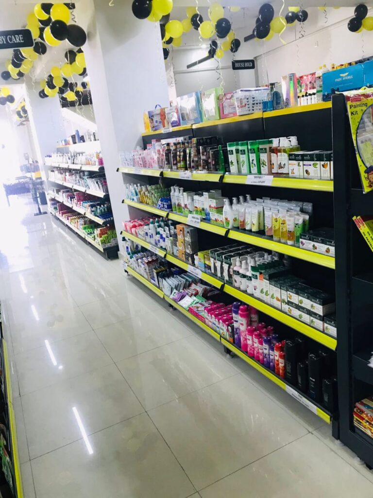 Display Racks for Shop in Dehradun Shelving and rack manufacturer in Ludhiana: Multiple rows of black shelves with bright yellow edges, stocked with various food products. Products: A wide variety of cereals, including recognizable brands like Kellogg's Many types of snacks, particularly corn-based snacks like tortilla chips Different flavors and brands of chips and crunchy snacks Some oatmeal and breakfast products Organization: The products are neatly arranged and grouped by type and brand. Signage: There's a small sign visible that says "CEREALS" indicating the product category. Decoration: The ceiling is decorated with balloons in black and yellow colors, along with some streamers. This suggests the store may be celebrating an opening, anniversary, or special event. Lighting: Bright fluorescent lights hang from the ceiling, providing ample illumination for the products. Layout: The shelves are arranged in an L-shape, with the corner of the aisle visible in the image.