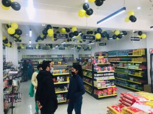 Display Racks for Shop in Dehradun Shelving: Multiple rows of black shelves with bright yellow edges, stocked with various food products. Products: A wide variety of cereals, including recognizable brands like Kellogg's Many types of snacks, particularly corn-based snacks like tortilla chips Different flavors and brands of chips and crunchy snacks Some oatmeal and breakfast products Organization: The products are neatly arranged and grouped by type and brand. Signage: There's a small sign visible that says "CEREALS" indicating the product category. Decoration: The ceiling is decorated with balloons in black and yellow colors, along with some streamers. This suggests the store may be celebrating an opening, anniversary, or special event. Lighting: Bright fluorescent lights hang from the ceiling, providing ample illumination for the products. Layout: The shelves are arranged in an L-shape, with the corner of the aisle visible in the image.