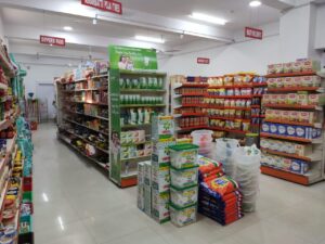 (Dukan Ke Racks) kirana store rack in Bhopal, Madhya Pradesh. Racks Manufactured by GKSP RACKING. It shows multiple aisles and sections. There are signs visible for different product categories like "DIAPERS/PADS" and "HEALTH & BEAUTY". The central area shows more Ariel detergent boxes and plastic containers. The overall impression is of a well-stocked, organized, and modern grocery store or supermarket.